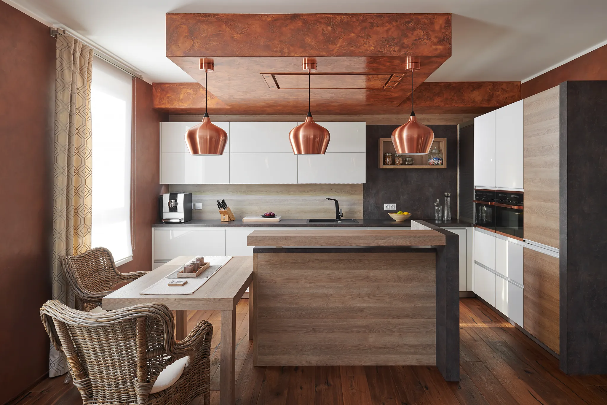 Luxusní moderní kuchyně v měděných a bílých tónech. Tři měděné závěsné lampy visí nad kuchyňským ostrovem s dřevěným obložením. Bílé lesklé skříňky kontrastují s tmavou pracovní deskou a dřevěnou podlahou. Proutěné křeslo v popředí dodává prostoru přírodní a útulný vzhled.