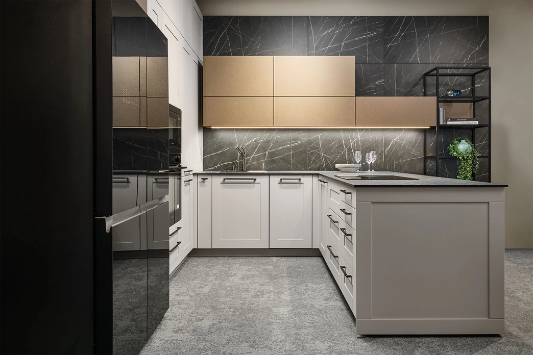 Moderní kuchyně do L s bílými spodními skříňkami, zlatými horními skříňkami, černým mramorovým obkladem, vestavěnými spotřebiči a kovovými úchytkami s podskříňkovým osvětlením ve studiu v Říčanech
