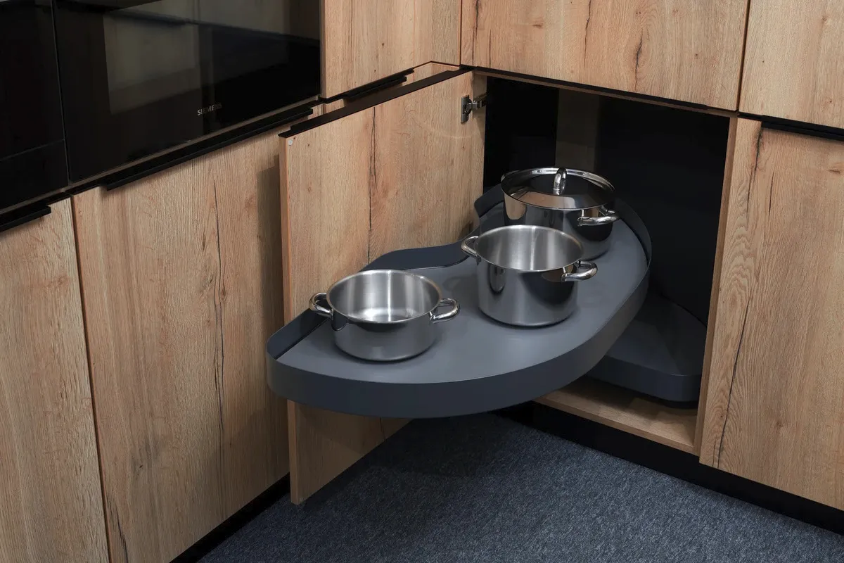 Výsuvný otočný kuchyňský systém s nerezovými hrnci uvnitř rohové skříňky s dřevěným dekorem.