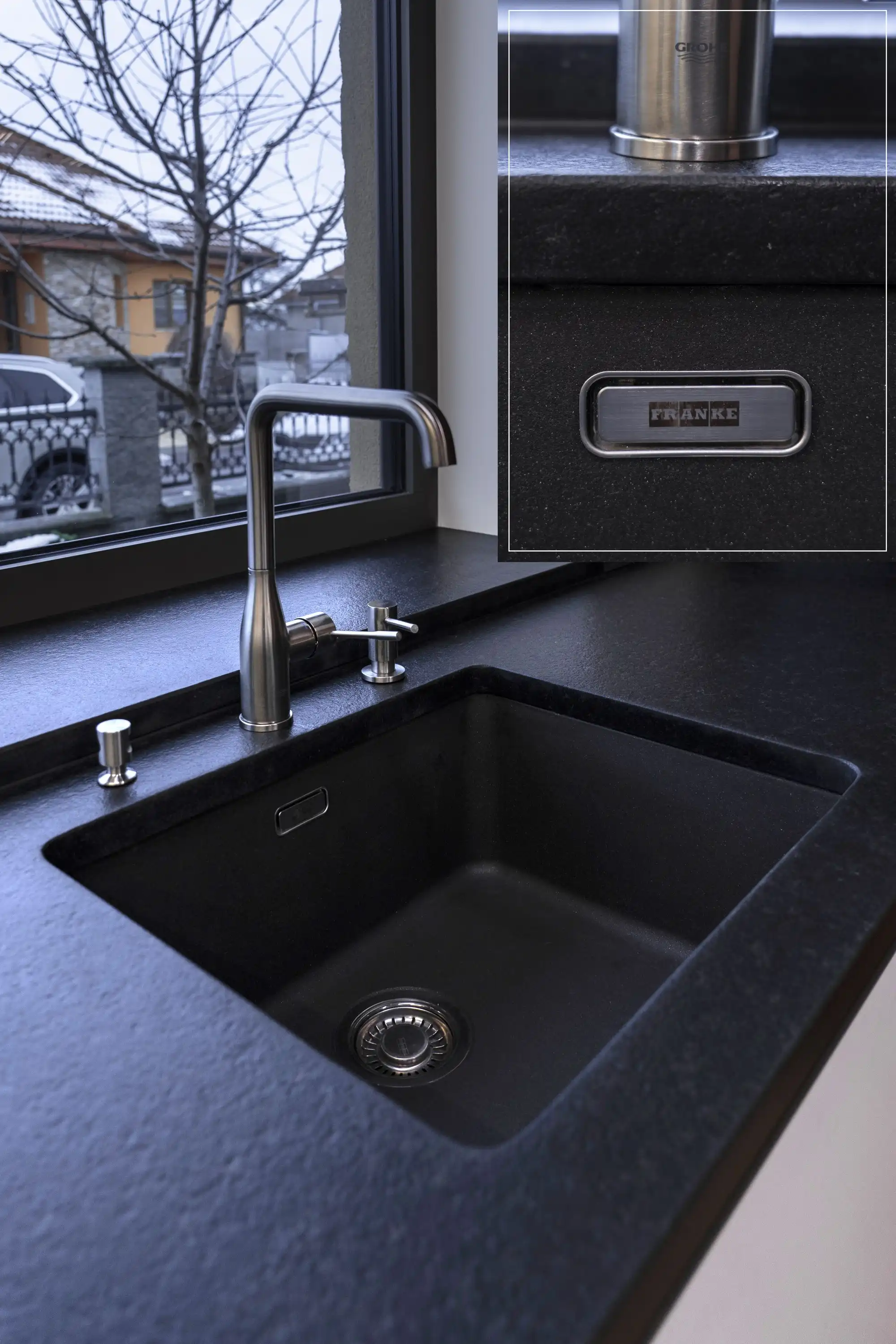 Černý granitový kuchyňský dřez Franke s moderní nerezovou baterií a dávkovačem saponátu, zapuštěný do pracovní desky u okna.