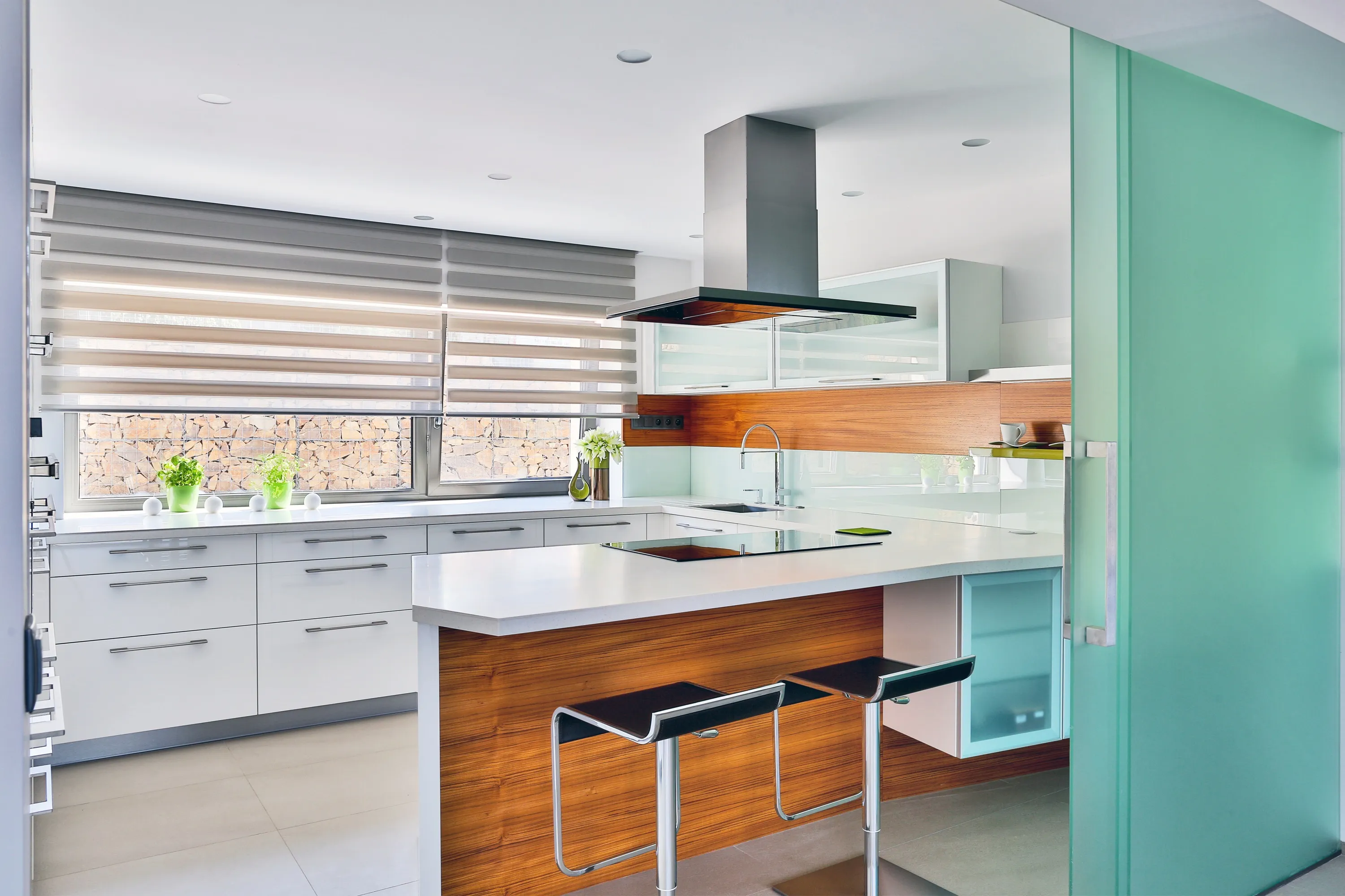 Moderní kuchyně s bílou linkou, ořechovým kuchyňským ostrůvkem, tyrkysovou akcentní stěnou a nerezovým odsavačem
