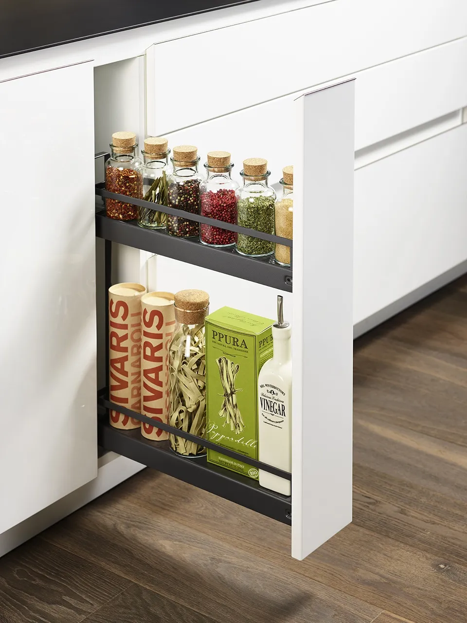 Úzká výsuvná kuchyňská skříňka s kovovým systémem na kořenky, oleje a suché potraviny, integrovaná do bílé moderní kuchyňské linky.